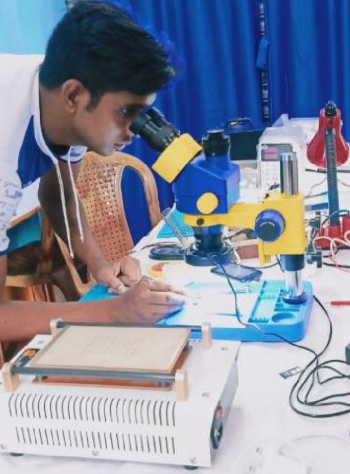 A student repairing a phone board under a microscope at SS TELECOM